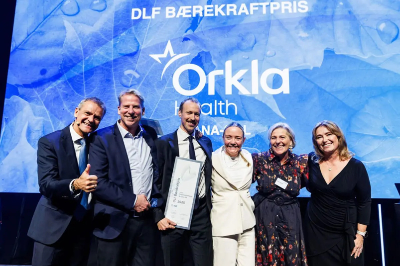 6 personer står på en scene, i pyntede klær, og holder opp en prisutmerkelse